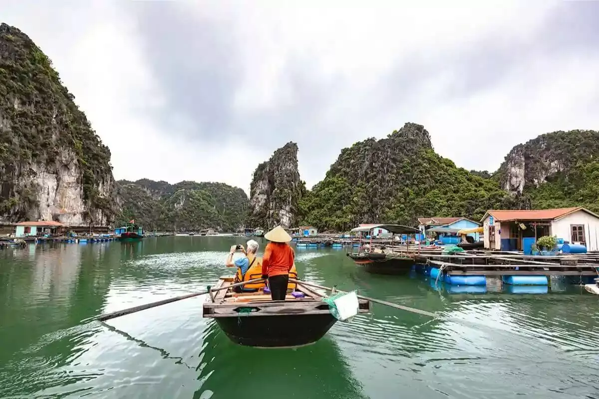 Bamboo boat ride through Cua Van Fishing Village waterways, passing colorful floating houses and fishing boats, Halong Bay Vietnam