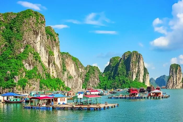 Cua Van Fishing Village — colorful floating homes on Halong Bay water surrounded by limestone karst cliffs, one of the last traditional floating communities in Vietnam