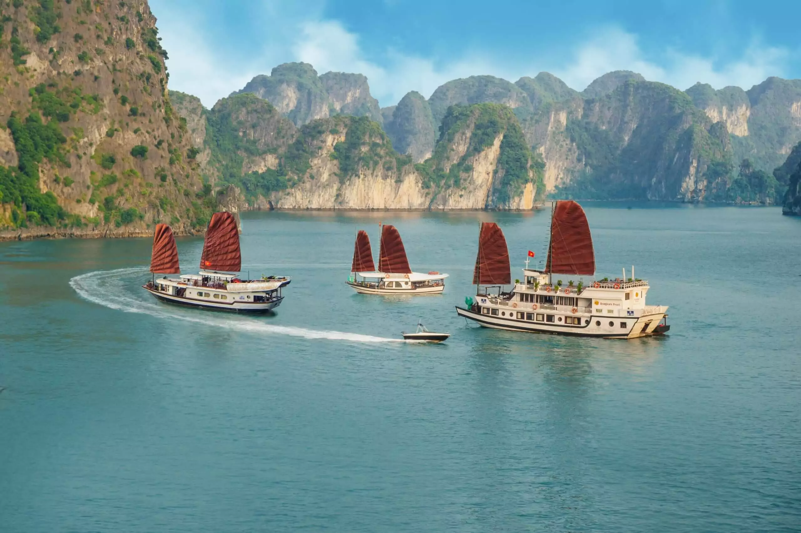 Halong Bay cruise junk boat sailing at sunset among limestone karst islands — traditional wooden vessel on Route 2 overnight cruise, Vietnam 2026