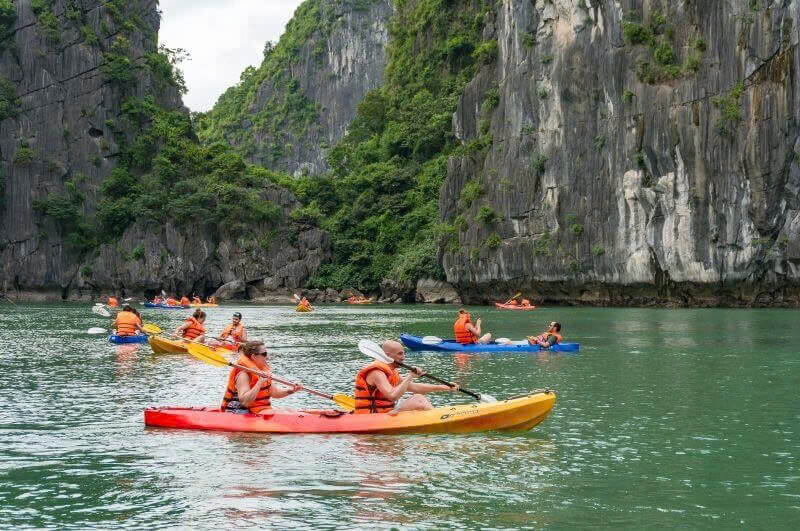 Guests kayaking at the Tra Bau area near Aurora Cruise, paddling between towering limestone cliffs in Lan Ha Bay