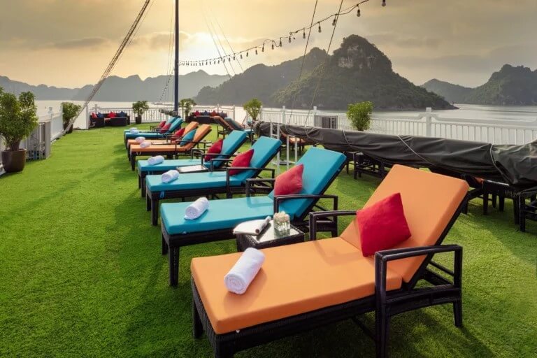 Aurora Cruise Sundeck with teal and orange chaise loungers at sunset overlooking Lan Ha Bay islands