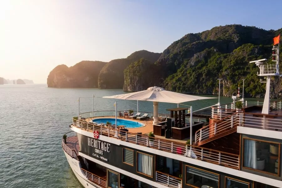 The Heritage Cruises Cat Ba - Vietnam branding on Heritage Binh Chuan Cruise, framed by Lan Ha Bay's karsts at sunrise.