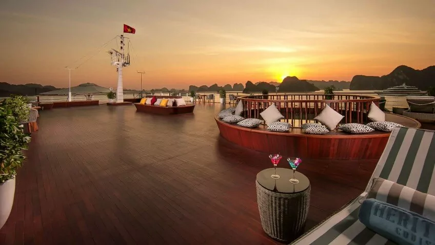 Round daybed seating on the sundeck of Heritage Binh Chuan Cruise, framed by a Lan Ha Bay sunset.