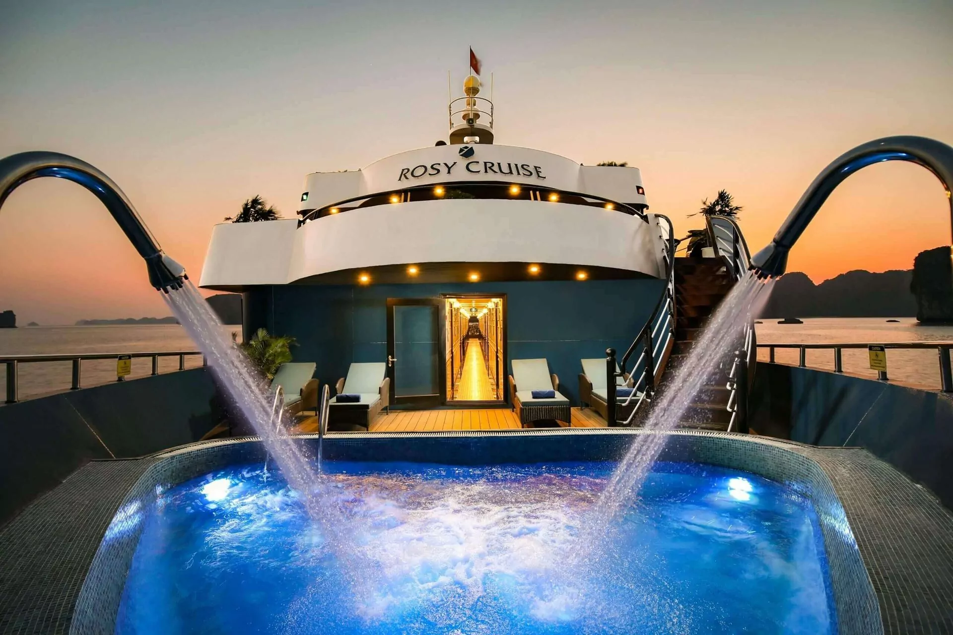The signature outdoor jacuzzi at the bow of Rosy Cruise, framed by Halong Bay's sunset sky.
