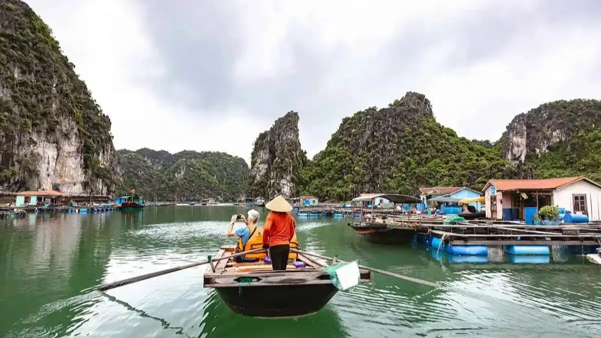 Bamboo boat ride through Cua Van Fishing Village waterways, passing colorful floating houses and fishing boats, Halong Bay Vietnam