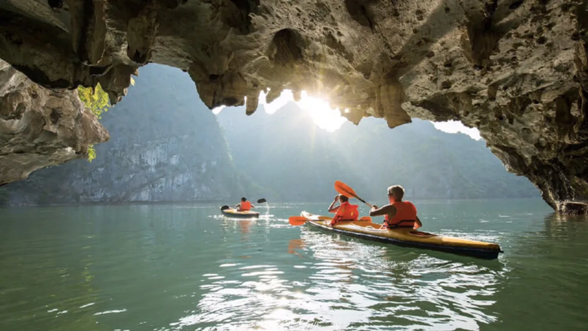 Bright Cave interior — natural sunlight filtering through limestone cracks illuminates the emerald water below, Dark and Bright Cave, Lan Ha Bay Vietnam