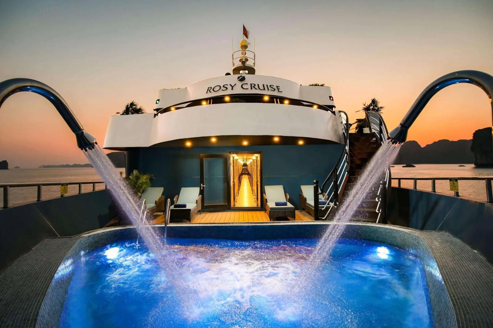The signature outdoor jacuzzi at the bow of Rosy Cruise, framed by Halong Bay's sunset sky.